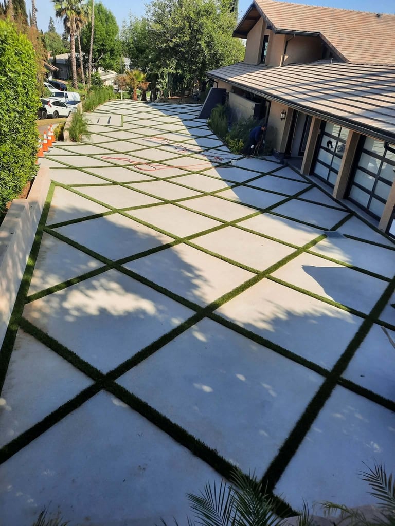 Modern driveway with large gray and white square pavers arranged in a grid pattern leading to a contemporary home with dark siding and garage