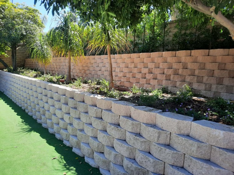 Concrete block retaining walls in a landscaped yard with green lawn and tropical plants